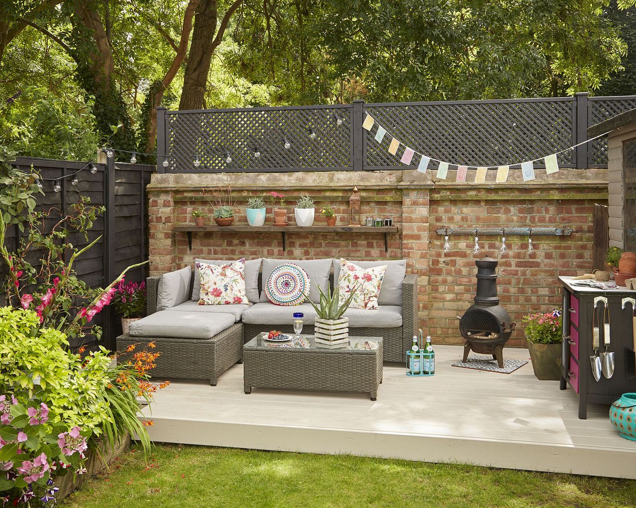 decked patio at the bottom a garden with a corner sofa and mandala style cushions with bright bunting