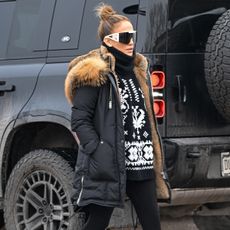 Jennifer lopez wears large sunglasses, a black turtleneck sweater, black fur-lined winter coat, and black leggings.