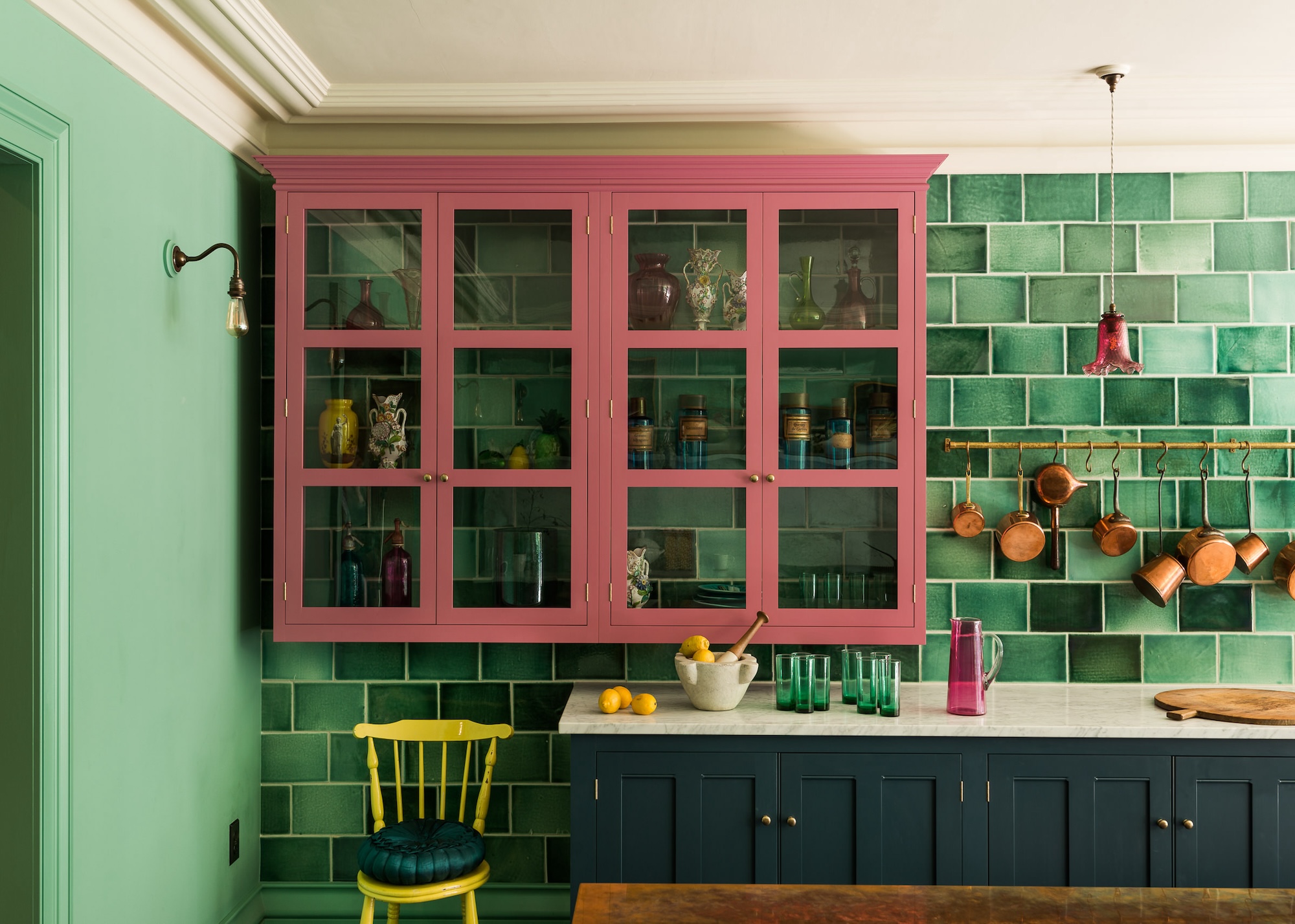 A colorful kitchen showing green Metro tiles stretching to the ceiling and behind a raspberry wall unit