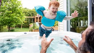 Young boy being thrown up in the air by his dad in a hot tub.