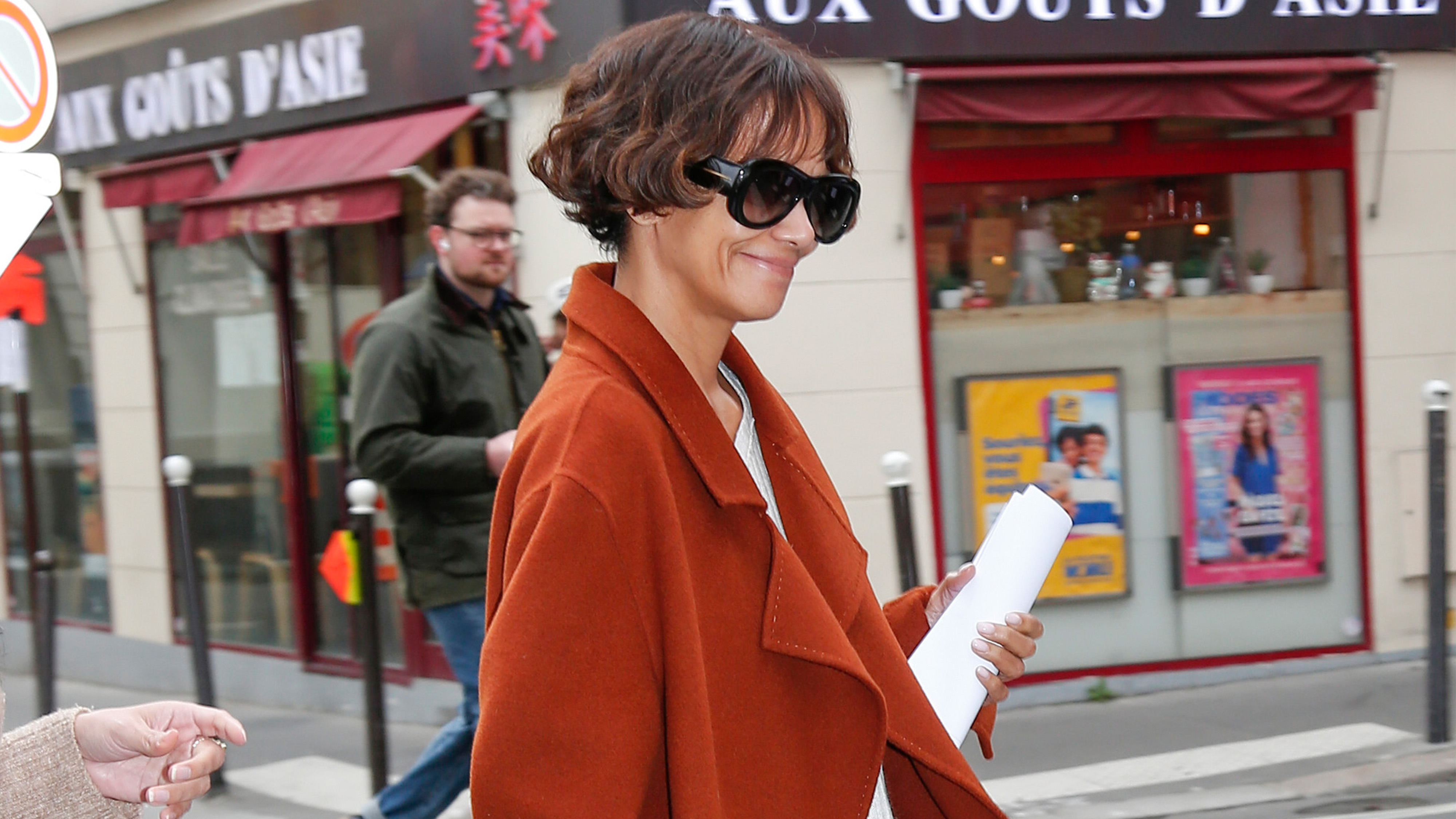Halle Berry wears oversize sunglasses and a rust-colored jacket.