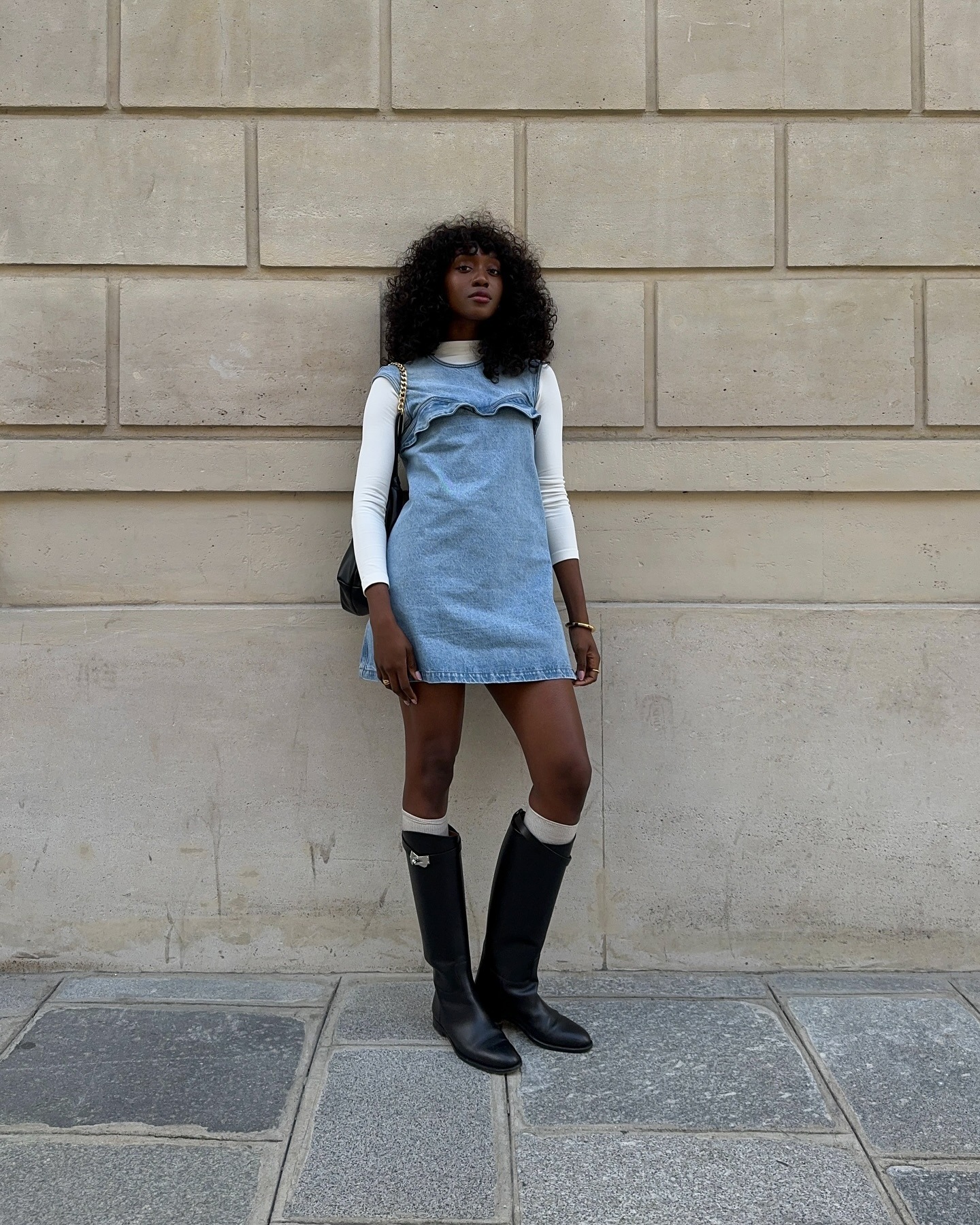 Frau trägt Jeans-Minikleid, cremefarbenen Rollkragenpullover und kniehohe schwarze Stiefel