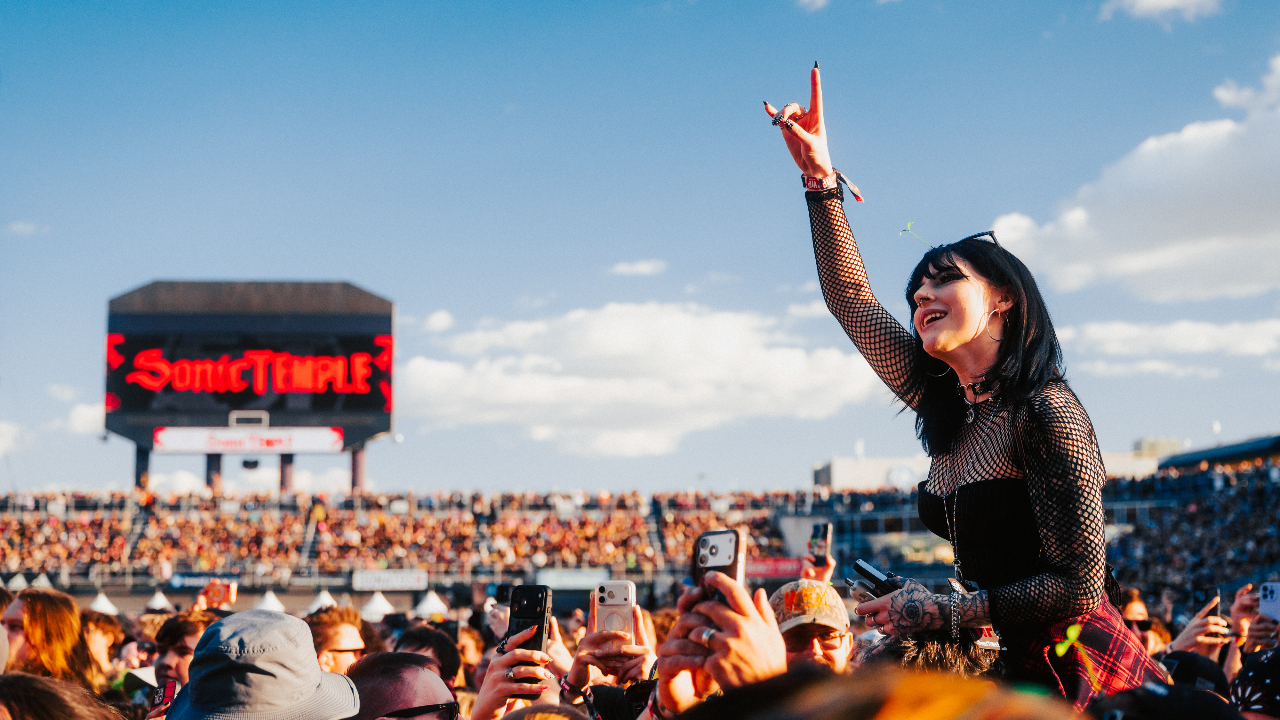 A woman on someone's shoulder raising the horns in a crowd