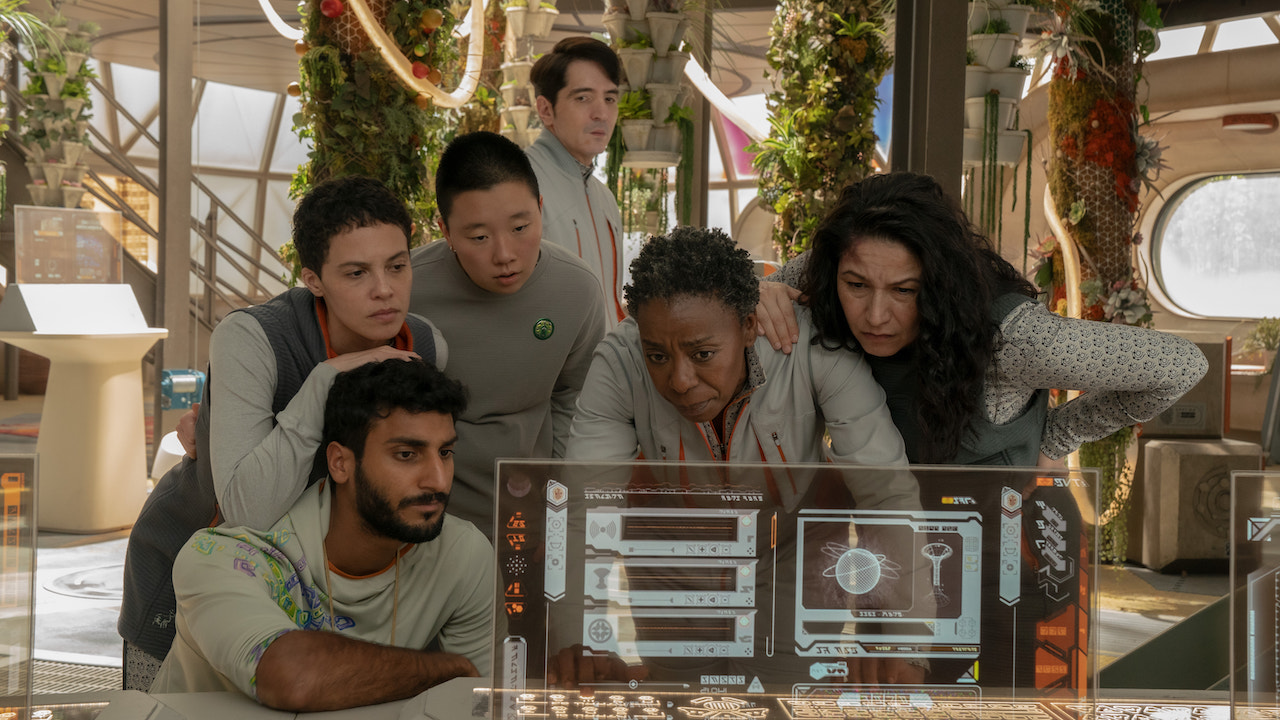 Mensah, Gurathin, Pin-Lee, Rathi, Bharadwaj, and Arada crowded around computer hologram in Murderbot Season 1