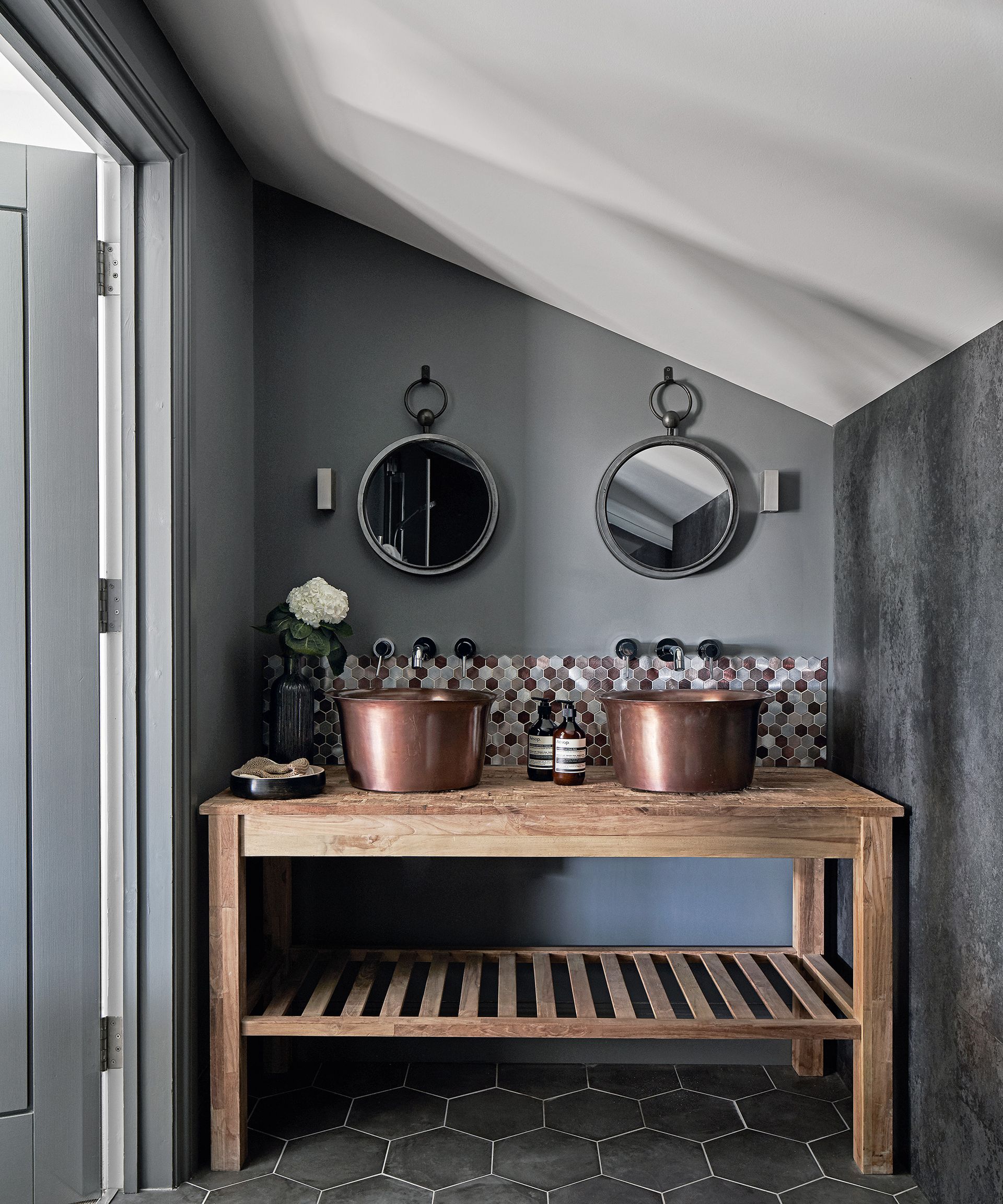 An example of bathroom color ideas showing a wooden double vanity with brass sinks in a gray bathroom