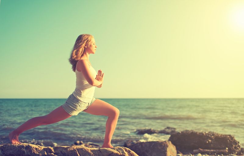 A woman does yoga near the ocean.