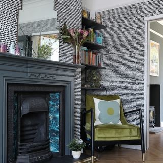 Wallpapered living room with dark fireplace and armchair in corner, furnished with hanging mirror and accent cushion