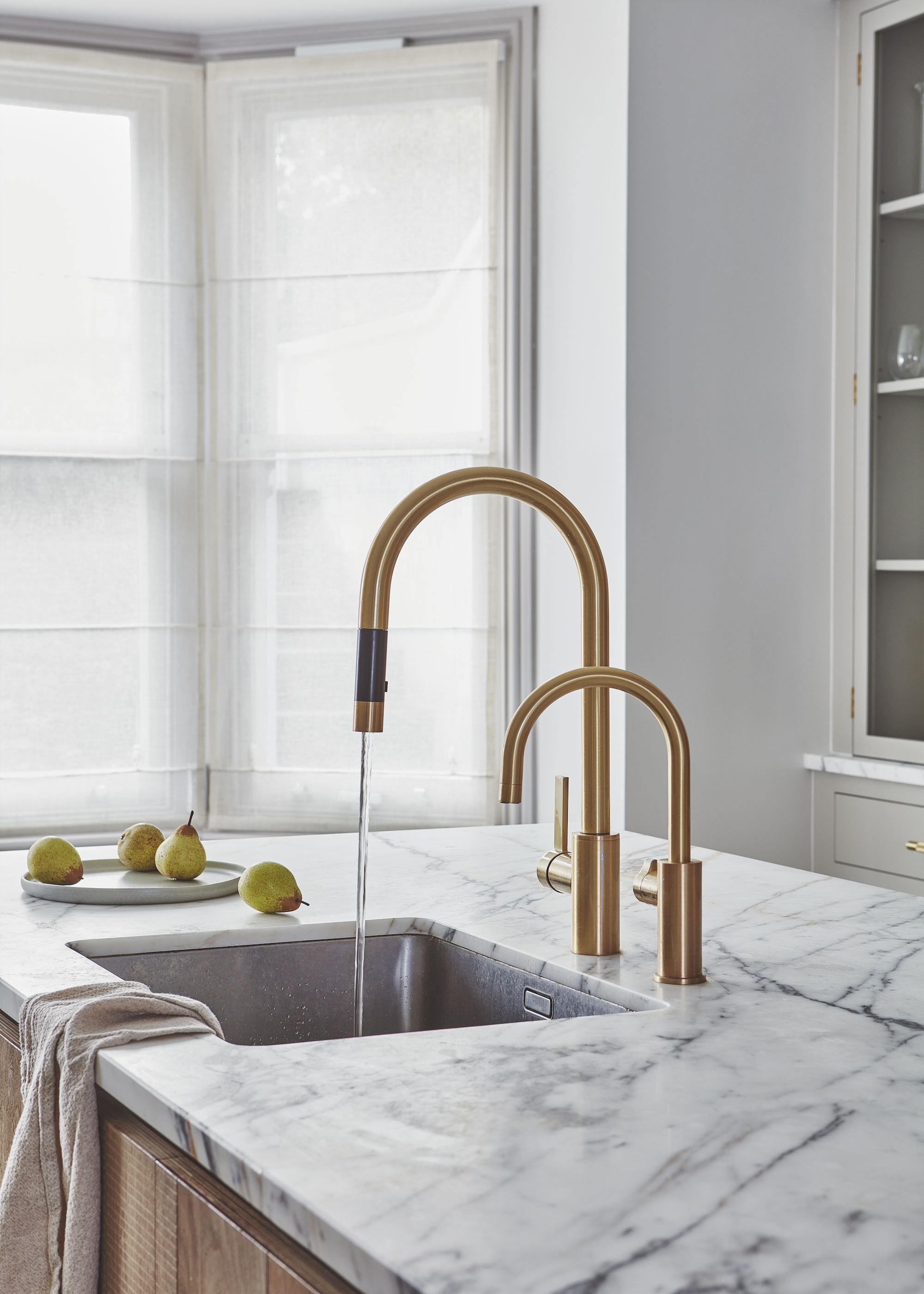 gold kitchen tap with a high arch spout and matching hot water tap shown on marble worktops and a built in kitchen sink