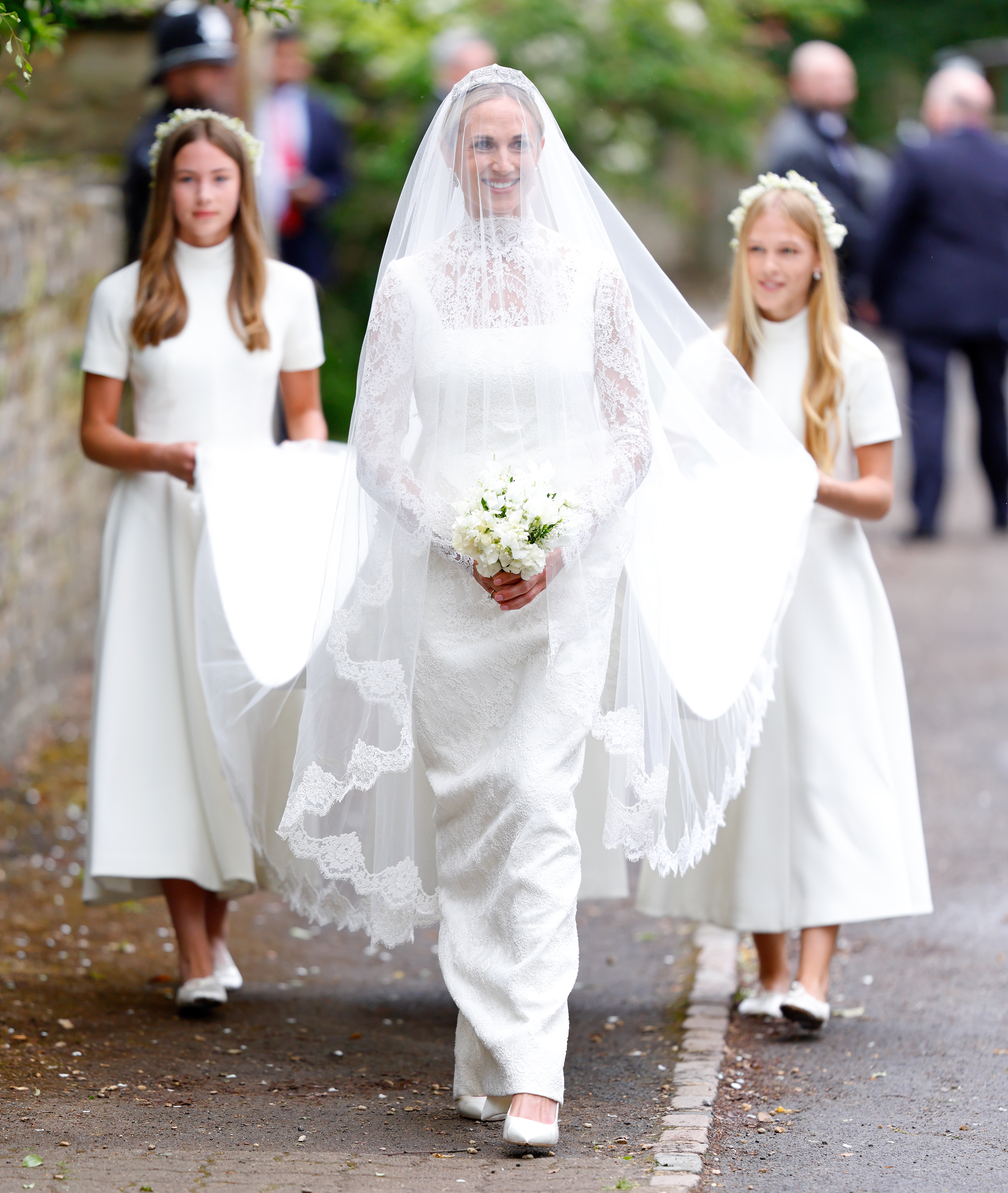 Harriet Sperling walking in her wedding dress with her daughter and stepdaughters holding the train