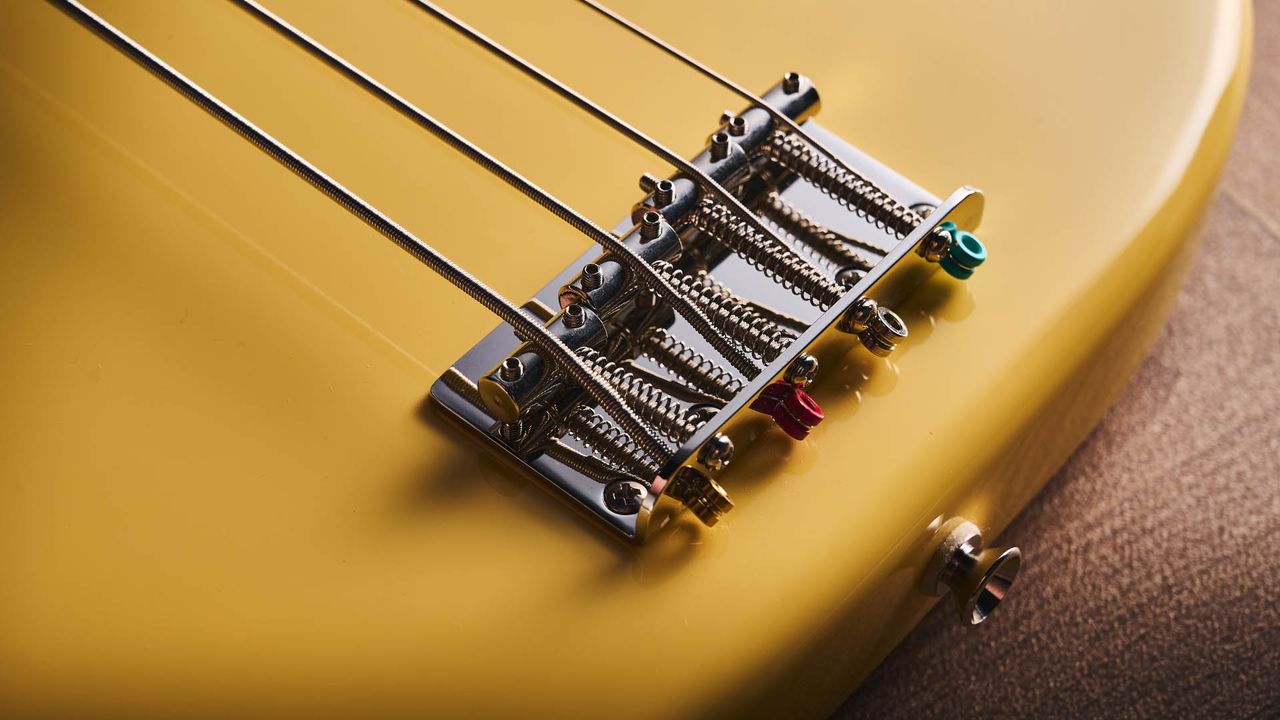 The Squier Classic Vibe Telecaster Bass is a fine-looking four-string in a custard-colored Vintage White, and is here photographed in close-up, against a plain wooden background. It has a single Wide Range humbucker.