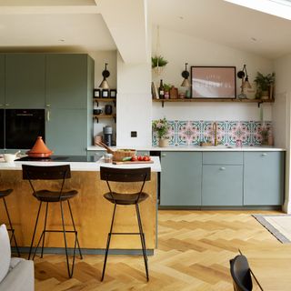 Light sage green kitchen with gold island and herringbone flooring.