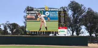 A high-quality, bright video board shows an LBSU Dirtbag college baseball player fielding a ground ball. 