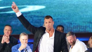 Rob Gronkowski holds a shot glass over his head on stage at The Roast of Tom Brady.