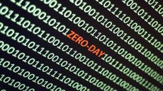 Lines of green binary code on a black screen, with zero day written in red in the middle