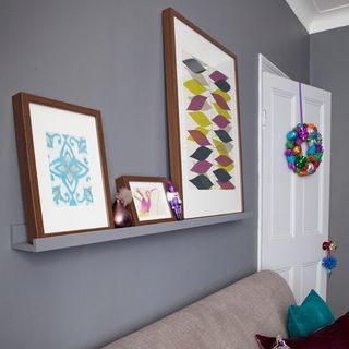 grey wall with frames on wall shelf and white door with wreath