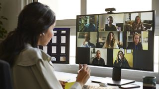 Woman wearing over ear headphones on a zoom work call with people on camera on screen.