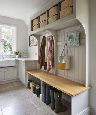 Laundry room storage ideas in a traditional neutral scheme with stone flooring, including a built in wooden boot bench