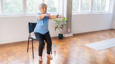 Senior woman practicing sit-to-stand exercise, a chair behind her