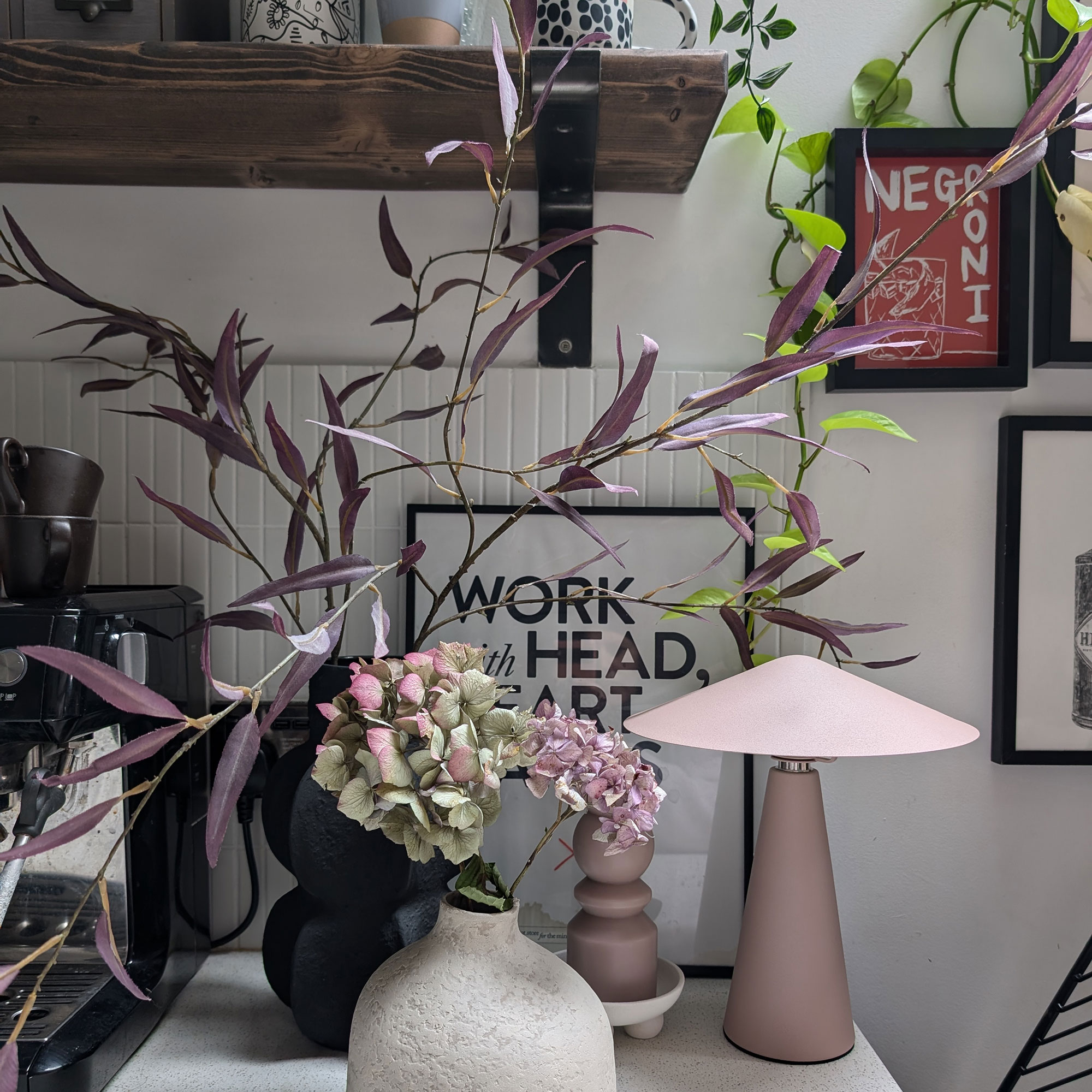 Corner of white kitchen countertop of vases of flowers and foliage and pink wireless lamp