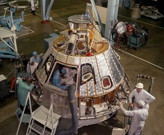 High angle view of Spacecraft 12 Command Module (for AS-204 mission, later renamed Apollo 1), looking toward -Z axis, during preparation for installation of the crew compartment heat shield, showing mechanics working on aft bay.