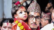 Nepal's appointed Royal Living Goddess, Aryatara Shakya, dressed inn red with a symbolic 'third eye' painted on her forehead, held by an adult man