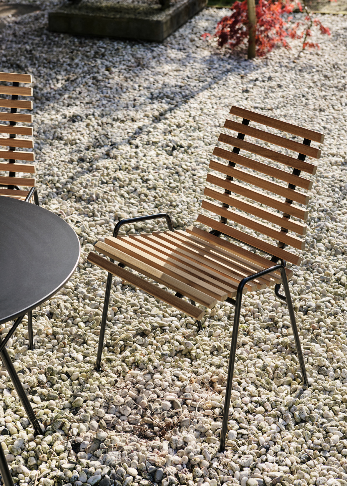 Wooden slatted chair sits on gravel next to black table