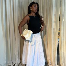 Influencer @nnennaechem wears a white long skirt, a black top, and a necklace. 