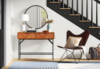a stylish wooden entryway console table with decor and a mirror behind it, with a chair and a dark black staircase, and a rug