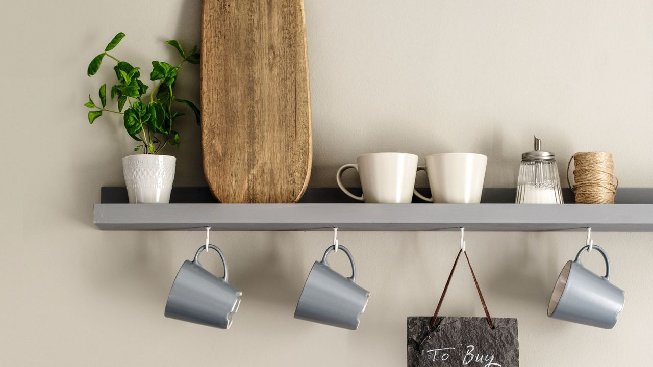 Two floating kitchen shelves with cup hooks and blue mugs, chopping board and blackboard, with storage jars with lids fixed below shelves