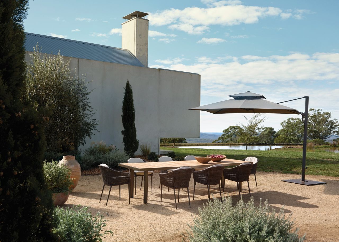 teak outdoor dining table in a modern gravel yard with a large shade umbrella