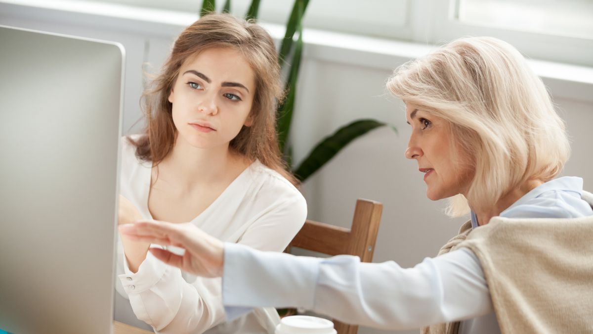 An older worker and her younger colleague having a discussion in front of a monitor