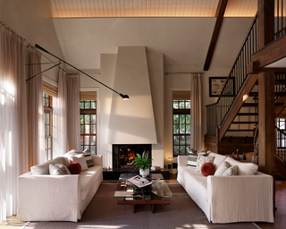 Lofty living room with tall fireplace heath behind coffee table surrounded by two white couches, featuring woods and notes from nature