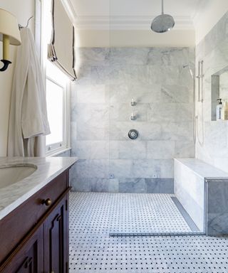 An example of how to design a bathroom showing a large walk-in shower with gray wall tiles and a shower seat