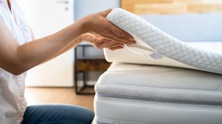 A woman lifts the edge of her white mattress topper placed on top of a white mattress