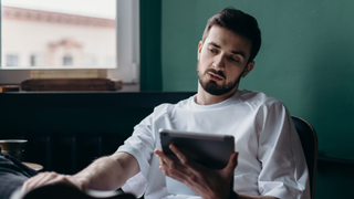 Glum looking man in white shirt holding iPad