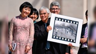 Vietnamese-US photographer Nick Ut (C) holds his Pulitzer and World Press Photo Award, 1972 photograph 'Napalm Girl', depicting Kim Phuc (L) as they attend Pope Francis' weekly open-air general audience in St. Peters' square on May 11, 2022 at the Vatican