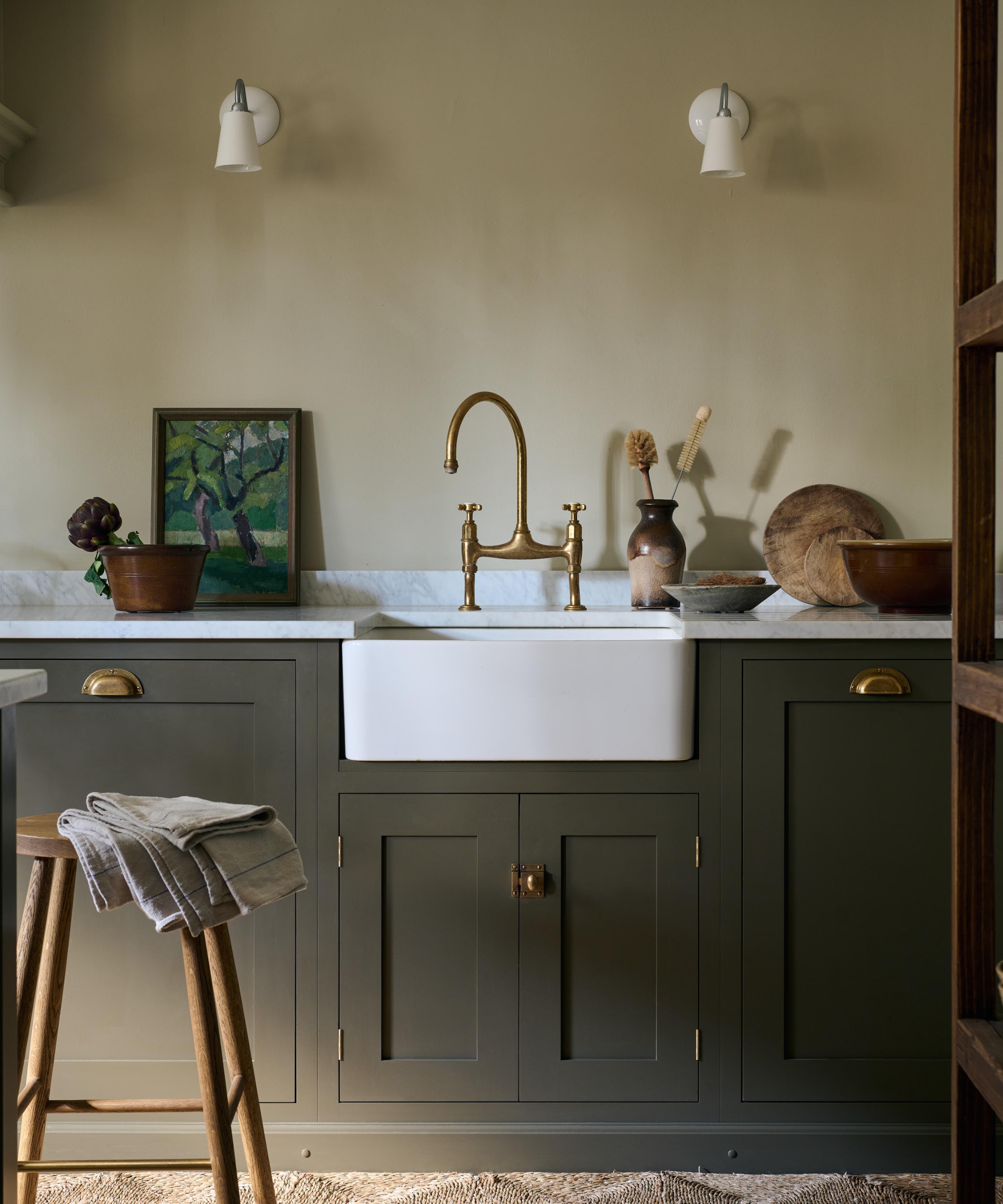 a traditional kitchen with dark green cabinets, warm neutral walls, marble countertops and a collection of vintage pieces decorating the counters