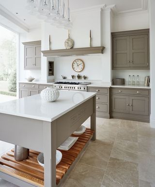 Mushroom gray cabinetry in an island kitchen layout idea with white walls and travertine flooring.