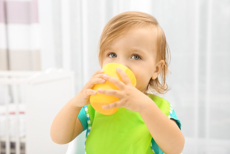 A little girl drinks juice from a cup.