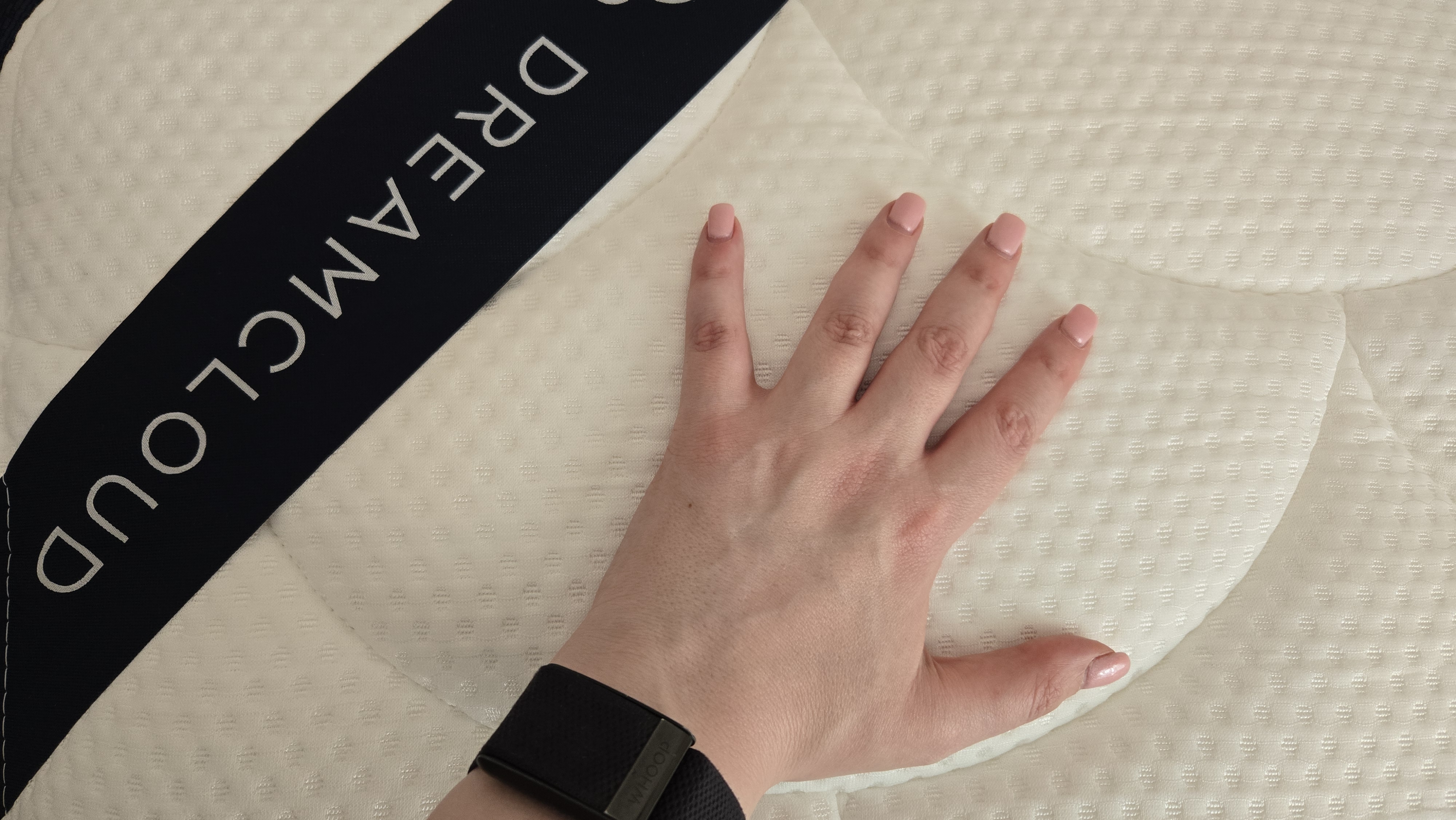 Manicured hand with a WHOOP Watch atop the cover of the DreamCloud Classic Memory Foam Mattress