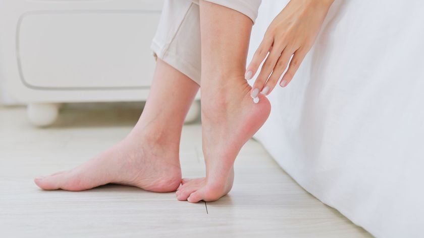 A woman&#039;s feet placed on the floor by a bed with her hand about to rub magnesium cream on them