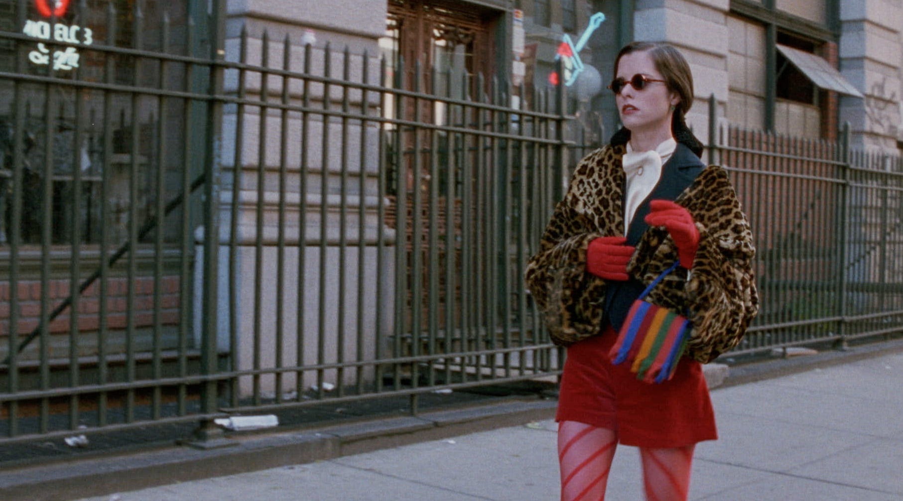 parker posey wearing red tights and a red skirt and leopard print coat walking down the street in party girl