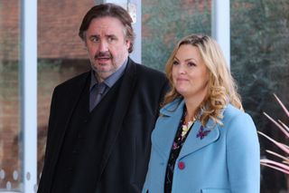 Shakespeare & Hathaway Season 4: Mark Benton and Jo Joyner in character as Frank Hathaway and Lu Shakespeare, standing in front of French windows, with Frank giving a quizzical aside glance