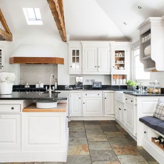 kitchen with stone tiled floor, white cabinetry and island, wooden ceiling beams