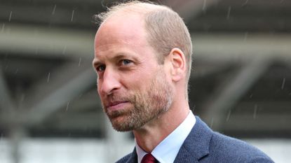 A closeup shot of Prince William wearing a blue suit and white shirt in the rain with a bemused expression 