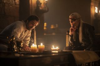 Fabien Frankel as Ser Criston Cole, Ewan Mitchell as Aemond Targaryen, sit in a candelit chamber in 'House of the Dragon'