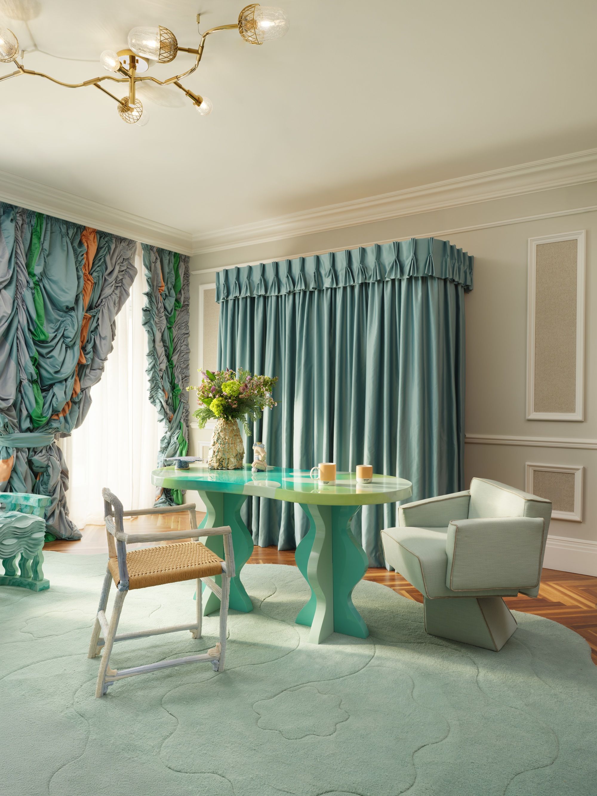 a hotel suite decorated with eclectic design ideas, including interesting draped curtains, a large rug and table and chairs, all in a celadon color