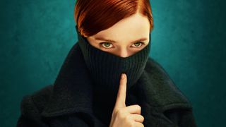 Lola Petticrew with a green turtleneck jumper covering the bottom half of her face, putting her finger to her lips