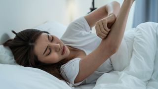 Woman in bed scratching arms