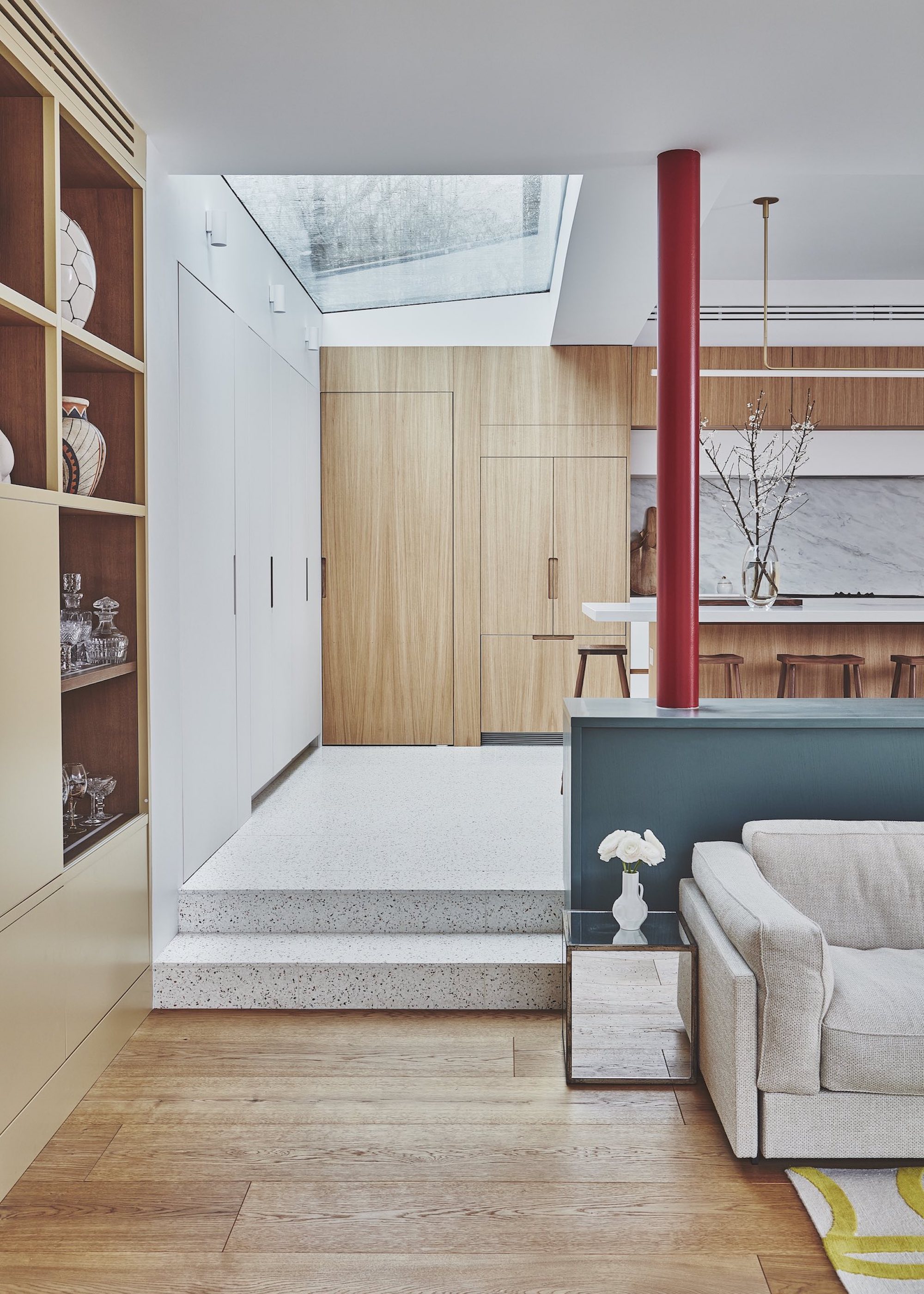 An open-plan kitchen extension with mixed flooring. There is a slight separation between the kitchen and living area. In the living area there is open shelving and in the kitchen are closed cupboards and cabinets.